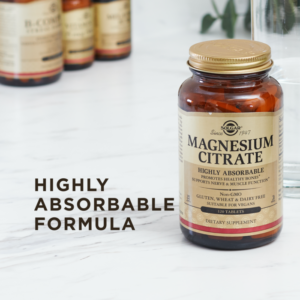An amber glass bottle of Solgar's Magnesium Citrate tablets sits on a marble surface. Two of the tablets are loose next to the bottle. Text reads "highly absorbable formula."