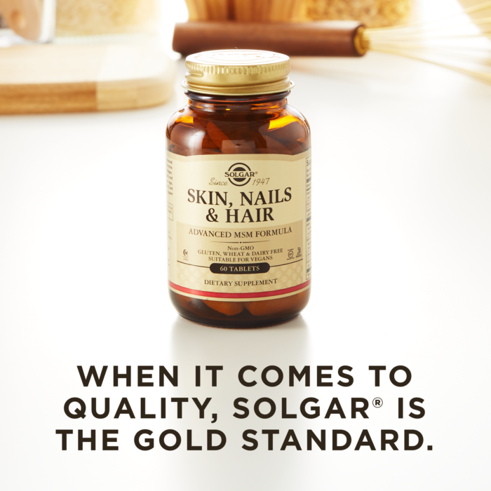A bottle of Solgar's Skin, Nails & Hair Tablets on a kitchen countertop. Text reads "When it comes to quality, Solgar is the gold standard."