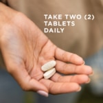 Two tablets of Solgar's Skin, Nails & Hair supplement held in an outstretched hand. Text says "take two tablets daily"