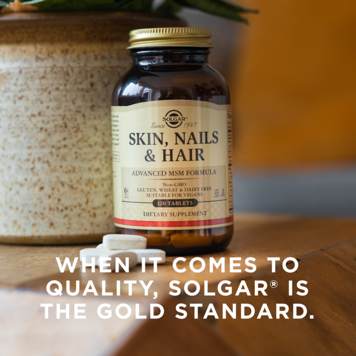A bottle of Solgar's Skin, Nails & Hair Tablets on a kitchen countertop. Text reads "When it comes to quality, Solgar is the gold standard."