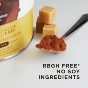 A spoon full of powder and three brown sugar cubes sit on a counter next to a container of Solgar's Whey To Go® protein powder in Chocolate flavor. Text overlaid reads "rGBH free*, no soy ingredients."
