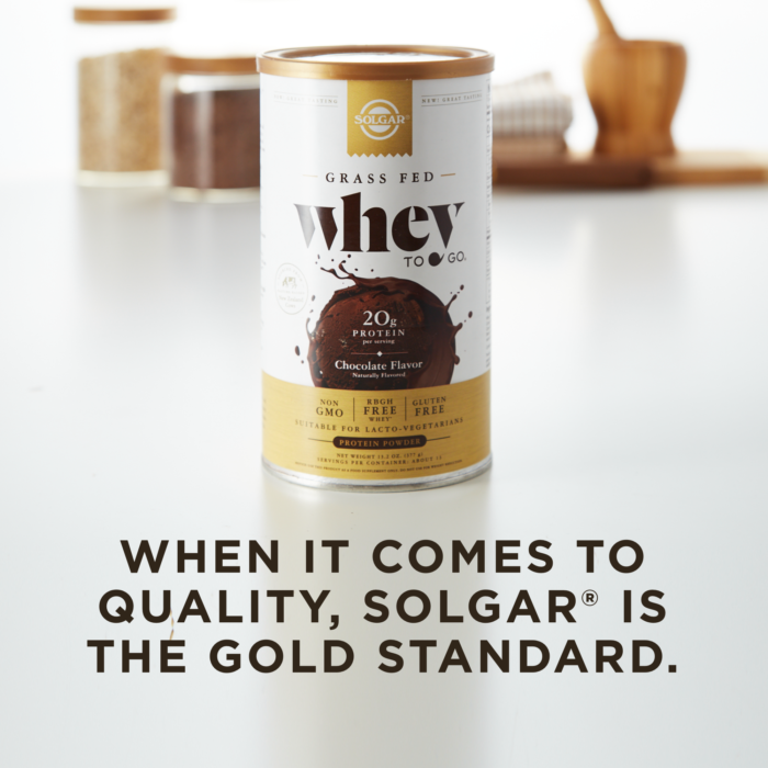 A container of Solgar's Whey To Go® chocolate-flavored protein powder on a kitchen counter, with text overlaid that reads 