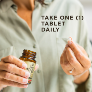 A woman holds a bottle of Solgar's Zinc Picolinate 22 mg Tablets in one hand and one of the tablets in the other. Text says "take one tablet daily"