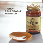 A bottle of Solgar's Zinc Picolinate 22 mg Tablets sits on a surface with a single tablet in a wooden dish next to it. Text reads "highly absorbable formula"