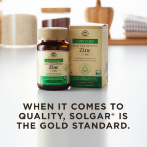 A bottle of Solgar's Earth Source Koji Fermented Zinc Vegetable Capsules next to its outer cardboard packaging on a clean surface. Text overlaid reads 'when it comes to quality, Solgar is the gold standard.'