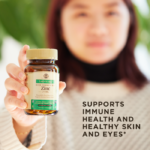 A smiling woman holds a bottle of Solgar's Earth Source Koji Fermented Zinc Vegetable Capsules up to the camera. Text overlaid reads 'supports immune health and healthy skin and eyes'