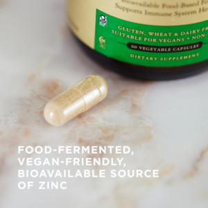 One transparent 25mg capsule of Solgar's Earth Source Koji Fermented Zinc on a marble surface. Text overlaid reads "food-fermented, vegan-friendly, bioavailable source of zinc."