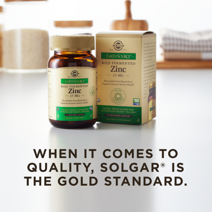A bottle of Solgar's Earth Source Koji Fermented Zinc Vegetable Capsules next to its outer cardboard packaging on a clean surface. Text overlaid reads 'when it comes to quality, Solgar is the gold standard.'
