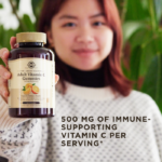 A smiling woman holds a bottle of Solgar's Adult Vitamin C Gummies up to the camera. Text overlaid reads '500mg of immune-supporting vitamin C per serving.'