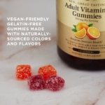 Four sugar-encrusted Solgar Adult Vitamin C gummies on a marble surface. Text overlaid reads 'vegan-friendly gelatin-free gummies made with naturally sourced colors and flavors'